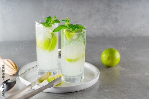 Cocktail mojito and bar accessories on gray background. Two highball glasses of mojito on a white plate. Summer cocktail with lime and mint