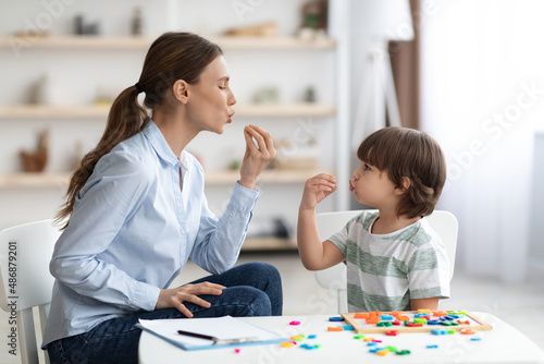 Young woman speech therapist studying together with small kid, learning practice pronunciation exercises with little boy