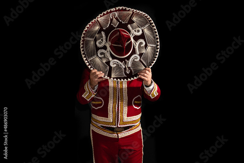 Mexican mariachi musician cover face with a sombrero on a black background