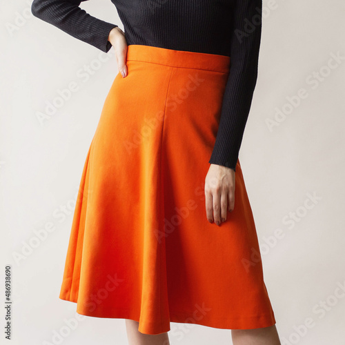 Young woman wearing an orange midi skirt and black blouse isolated on white background.