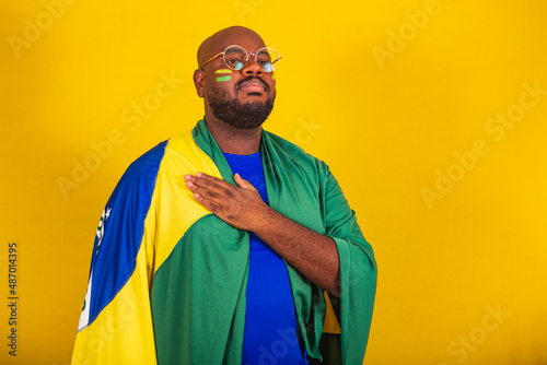 handsome afro brazilian man wearing glasses, brazilian fan, brazil, world cup 2022, hand to chest, singing anthem is born. Brazilian music. beloved homeland. patriot.