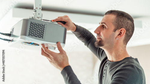 A man independently installs a multimedia video projector for a home theater or presentations on the ceiling.