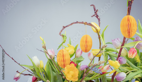 Wielkanocny bukiet wiosennych kwiatów z gałązkami i papierowymi jajkami na grafitowym tle.