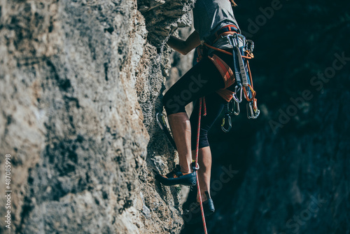 Detail of climb gear and equipment attached to a woman climbing harness while she climbs a route