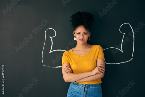 I am a strong woman. Shot of a woman posing with a chalk illustration of flexing muscles against a dark background.