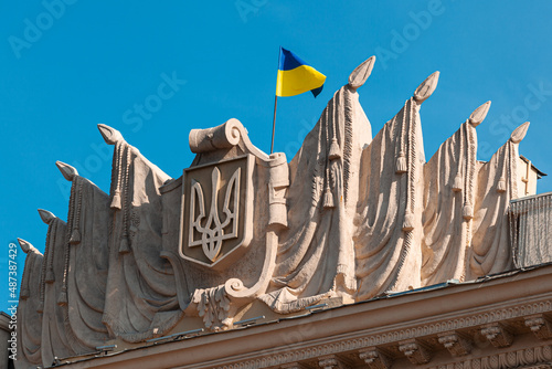 The national flag of the state of Ukraine flutters in the wind on top of the facade of an old building Kharkiv ODA. Yellow-blue flag. National emblem of Ukraine. Ukraine under attack.