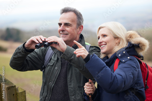 Mature Couple On Walk In Winter Countryside Looking At Wildlife Through Binoculars