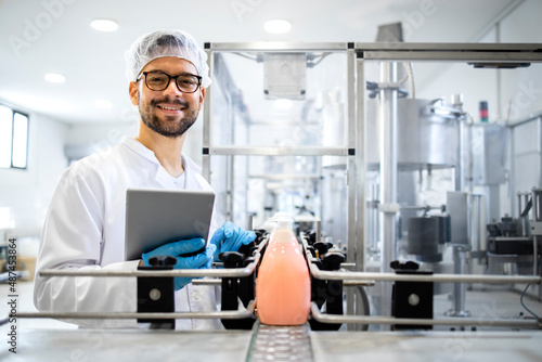 Production line worker or technologist standing by the automated conveyor machine with liquid soap products and cleaning chemicals.