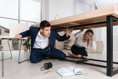 Scared employees hiding under office desk during earthquake