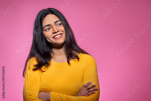 Portrait of a happy young woman looking elsewhere with hands crossed