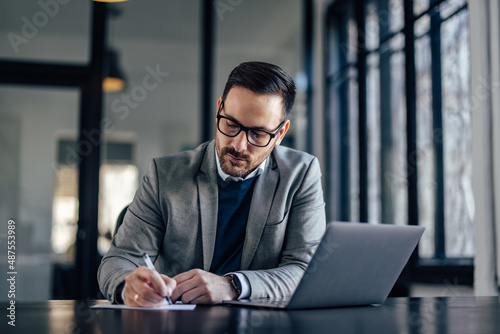 Focused caucasian executive, copying his notes from the laptop.