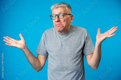 Middle age man over blue background clueless and confused expression with arms raised