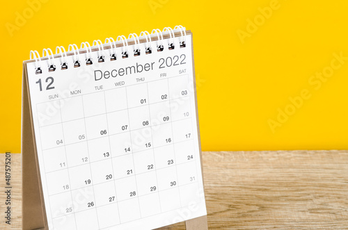 December 2022 desk calendar on wooden table with yellow background.