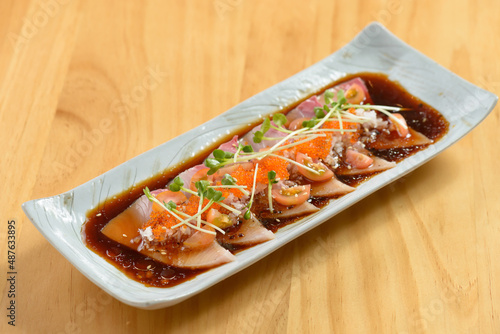 Fish Hamachi Carpaccio with chili sauce in a white tray on wooden background top view of japanese food