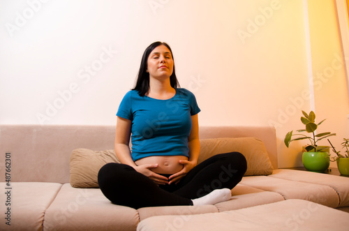 Young pregnant woman practicing breathing techniques , yoga or meditation in her living room 