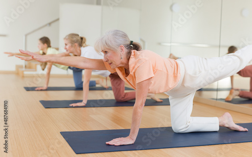 Active senior woman exercising stretching workout and incline during yoga class in fitness studio