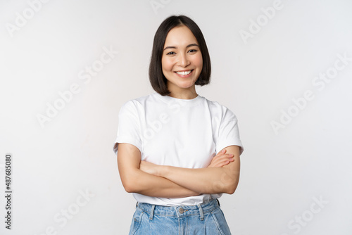 Portrait of happy asian woman smiling, posing confident, cross arms on chest, standing against studio background