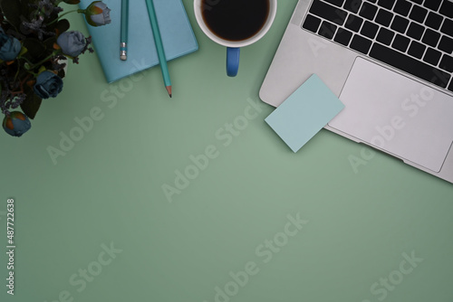 Computer laptop, coffee cup and notebook on green pastel background.