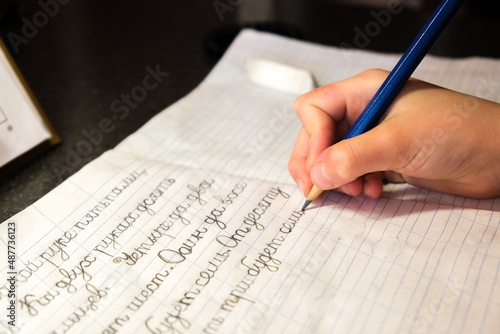 The child learns to write letters and words with a pencil in a notebook in Russian. The schoolboy writes close-up. Pencil in a child's hand. A little boy is learning to write Russian letters at the