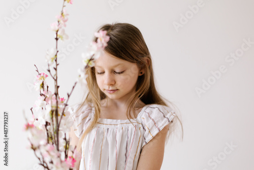 portrait of a beautiful innocent little girl holding a bunch of peach blossom twigs on a white background