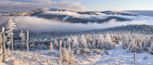 Through the valleys, the fog climbs the snow-capped mountain range of the Snieznik Massif just before sunset, the view from the top of Czarna Gora in winter.