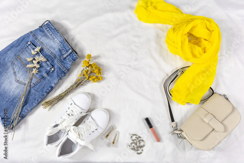 Blue jeans and jacket, bag and white sneakers on white bed. Women's stylish summer or spring outfit. Trendy fashion clothes. Flat lay, top view.