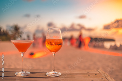 Two cocktail drinks with blur beach party people and colorful sunset sky in the background. Luxury outdoor leisure lifestyle, relaxing and romantic colors, blurred people partying on a summer evening