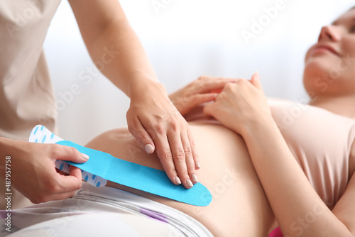 Physiotherapist applying kinesio tape on pregnant woman's belly