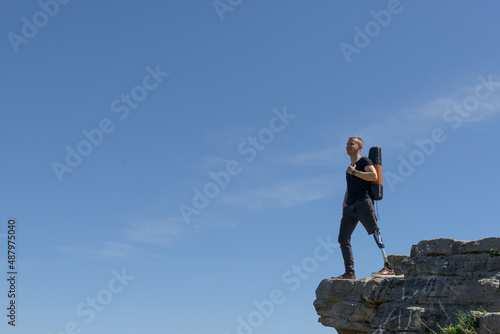 a man on a prosthetic leg travels the mountains. Dressed in black jeans and a T-shirt, he carrying mat