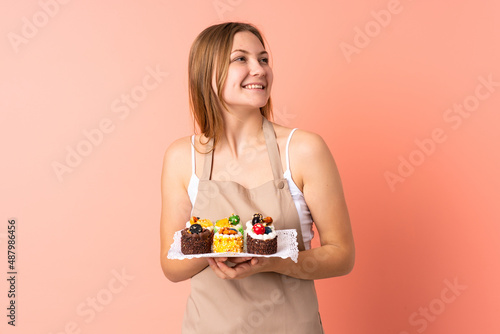 Pastry Ukrainian chef holding a muffins isolated on pink background laughing and looking up