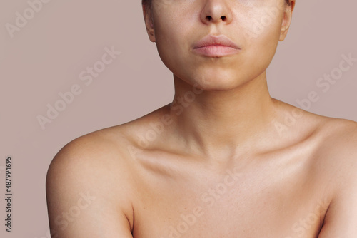 Cropped shot of a young caucasian tanned woman with a protruding collarbone isolated on a beige background. Body care, cosmetology. Soft delicate skin. Bronze skin, self-tanning, solarium. Close-up
