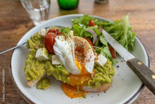 Sourdough toast, poached eggs, avocado pulp and fresh vegetables on plate in cafe, close up