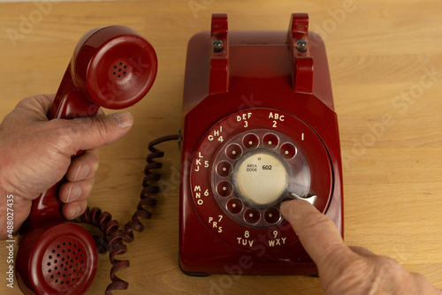 A man using a vintage red rotary telephone