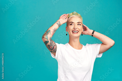 Rock your crown like the queen you are. Studio shot of a young woman putting a crown her head against a turquoise background.