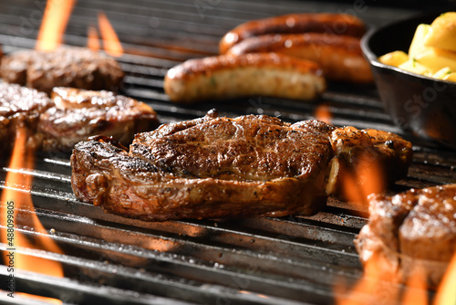 Cooked juicy steak meat beef with seasoning on a flaming grill surrounded by other meat and sausages.