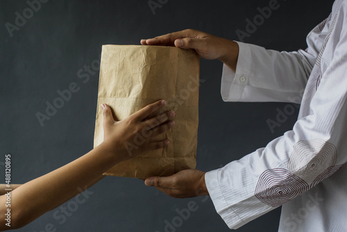 Side view of Muslim hands sharing rice alms bags isolated on black background.