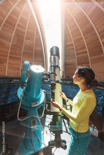 Happy woman in a space observatory looks at a meteorite or the sun through a professional optical telescope. Astronomy occupation and study concept