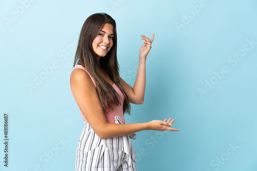 Young brazilian woman isolated on blue background extending hands to the side for inviting to come