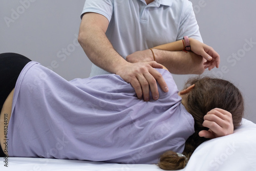 A chiropractor palpates the area of the scapula on the back of the patient. Appointment with an osteopath. The girl lies on the couch, the doctor works with her back. Back view