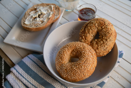 Three types of bagels with cream cheese and honey ona white wood table