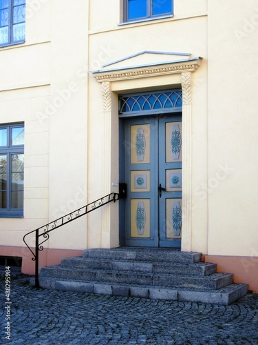 The entrance to the building consists of a double-leaf door, painted in gray and yellow, with a painting, a transom window, a portico, an elegant medieval-style handrail and a porch of four granite st