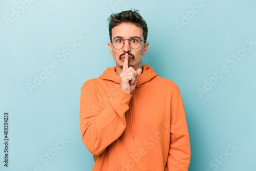 Young caucasian man isolated on blue background keeping a secret or asking for silence.