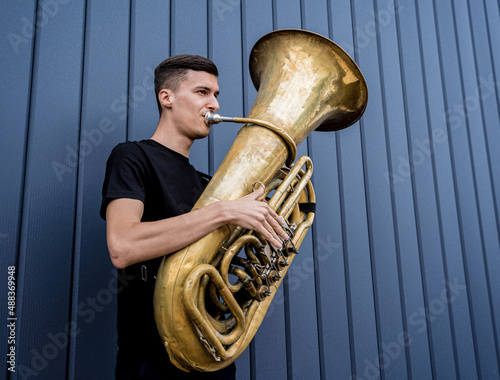 Young street musician playing the tuba near the big blue wall