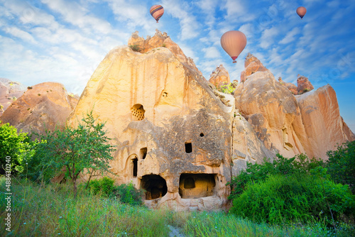 Rock monastery in the Zelve valley under blue sky with hot air balloons
