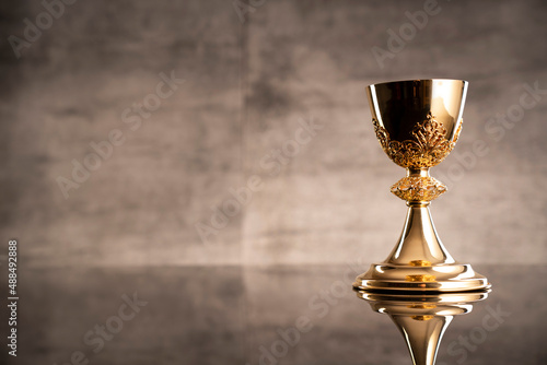 Catholic religion concept. Catholic symbols composition. The Cross, monstrance, Holy Bible and golden chalice on wooden altar and gray background. 