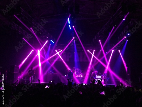 Pink and blue lights above the stage. Laser show at a live performance. Gig, concert. Strobe lights. Stage, scene. Perform. Live show. Purple rays. Spotlight. Festival. Violet gradient. Band. Fans