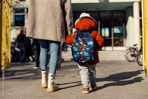 A mother entering the kindergarten yard with her preschooler boy.