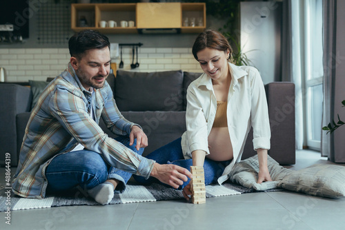 Young couple, man and pregnant woman, playing board game of jang together, sitting on the floor at home, having fun together