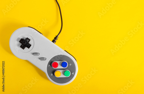 Photo of classic gray colored 8 bit game pad controller laying on yellow background.