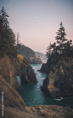 Sunset on natural bridges along the west coast of the Pacific Ocean, Oregon during the golden hour sunset - the sun's rays through the trees with dense vegetation. Beautiful seascape with rocks.
